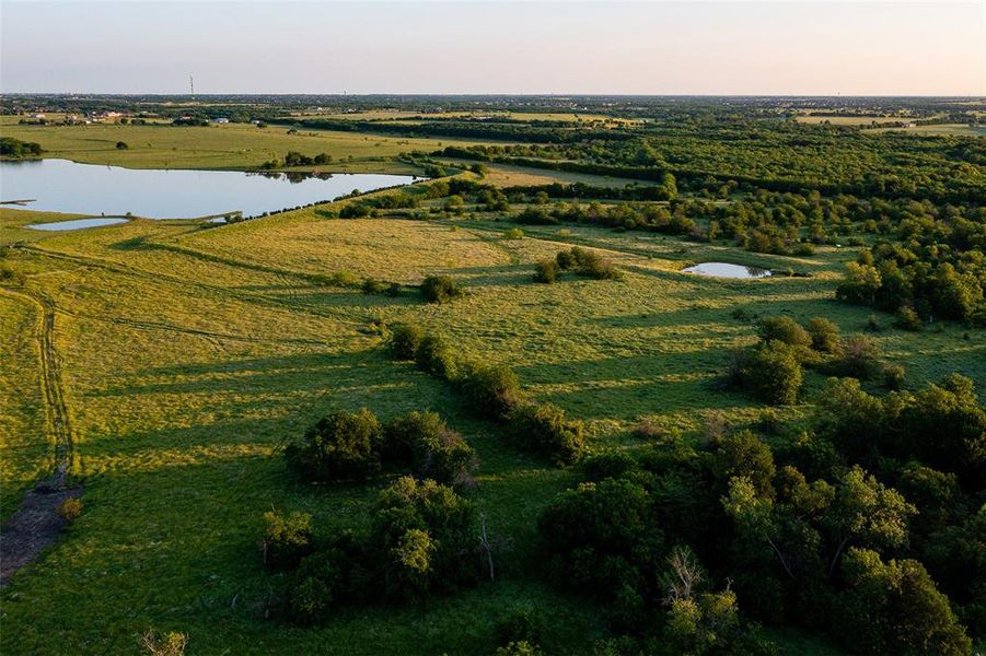 Expansive land featuring a large body of water, green grassy fields, and areas of mature trees