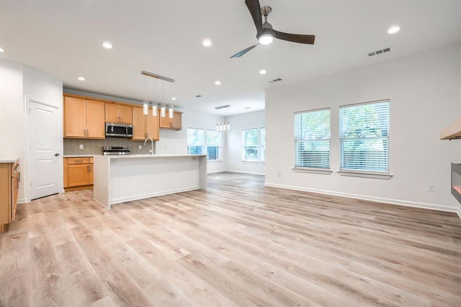Kitchen with open floor plan, decorative backsplash, recessed lighting, an island with sink, and light wood-style flooring