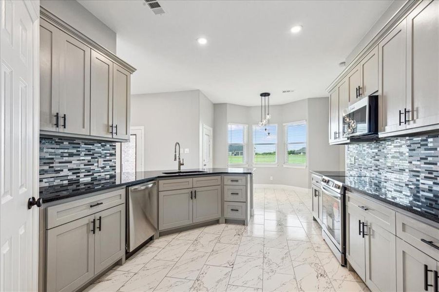 Kitchen featuring visible vents, a peninsula, marble finish floor, stainless steel appliances, and a sink