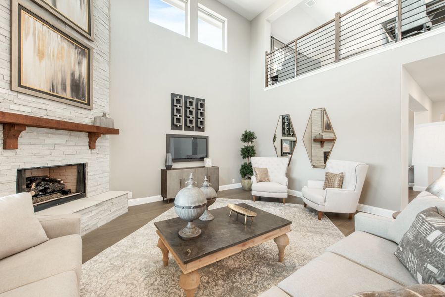 Living room with two-story ceiling, stone fireplace, white seating, and open loft railing above