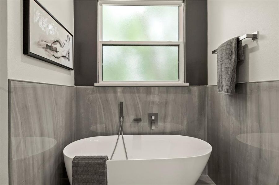 Full bathroom featuring a freestanding bath, tile walls, a sink, and wainscoting