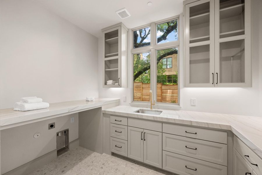 A sun-filled laundry room features ample counter space, sophisticated cabinetry, and a deep sink. A sun-filled laundry room features ample counter space, sophisticated cabinetry, and a deep sink.