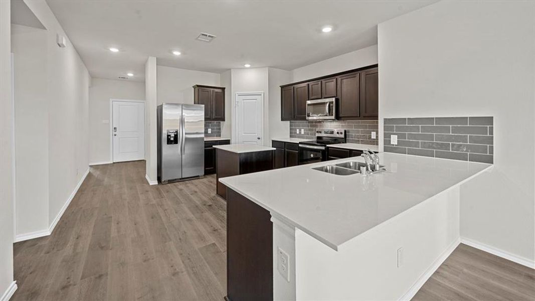 Kitchen featuring stainless steel appliances, dark wood finish cabinetry, a peninsula, light wood-type flooring, and decorative backsplash