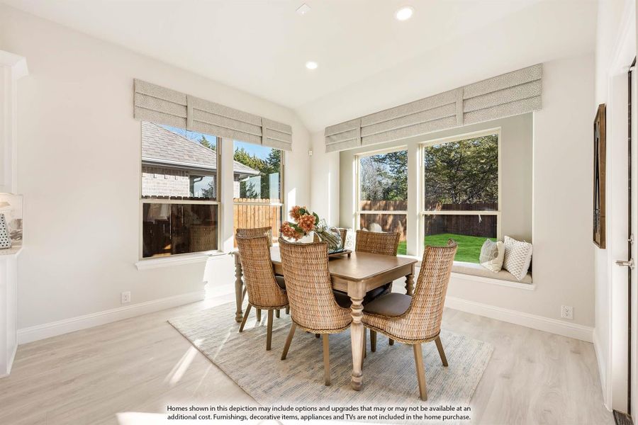 Bright dining area with wood table, wicker chairs, window seat, and large windows overlooking backyard