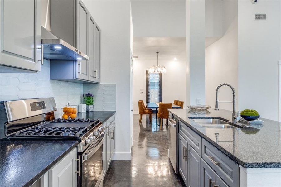 Kitchen featuring tasteful backsplash, appliances with stainless steel finishes, sink, hanging light fixtures, and wall chimney exhaust hood