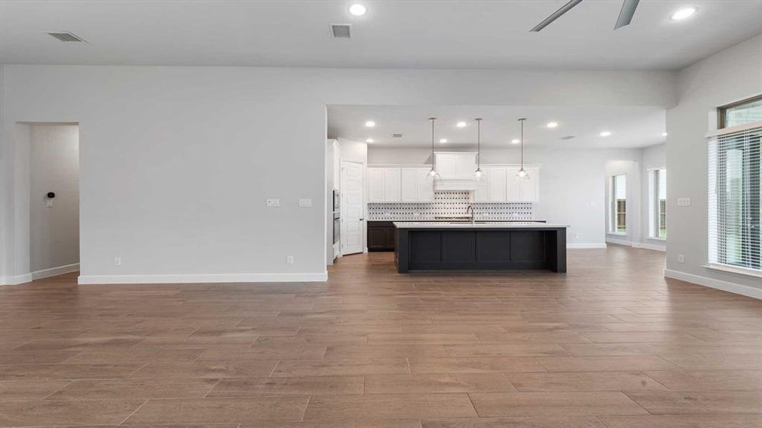 Kitchen featuring white cabinets, light hardwood / wood-style flooring, ceiling fan, an island with sink, and decorative light fixtures