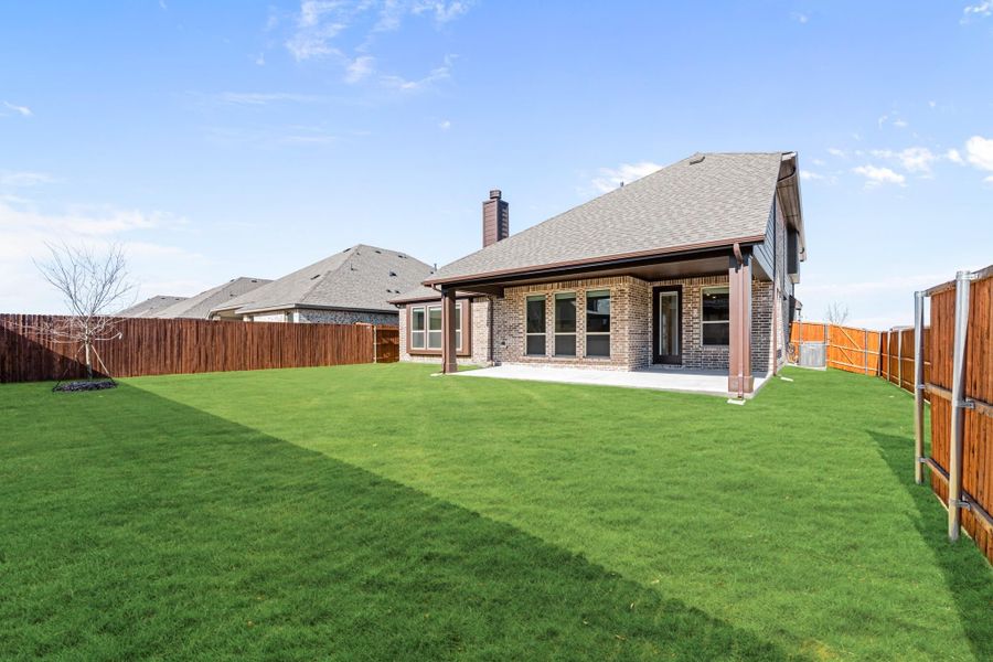 Brick home rear exterior with covered patio, large green lawn, and wood privacy fence
