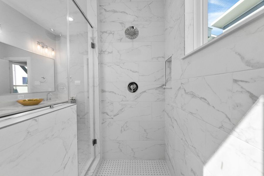 Spa-inspired walk-in shower featuring full-height marble-look tile, sleek glass enclosure, and a built-in niche for added functionality, creating a clean and luxurious feel.