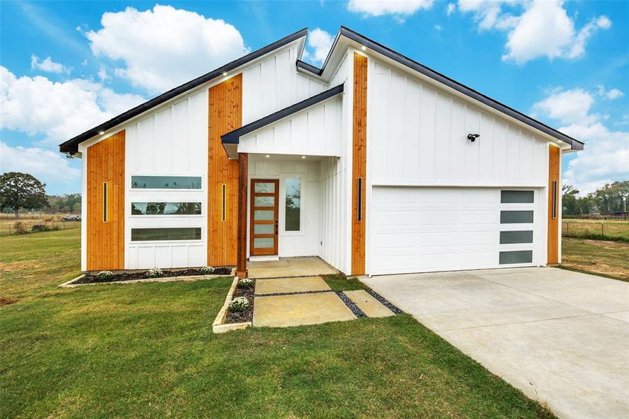 View of front of property with a front yard, driveway, board and batten siding, and a garage View of front of property with a front yard, driveway, board and batten siding, and a garage
