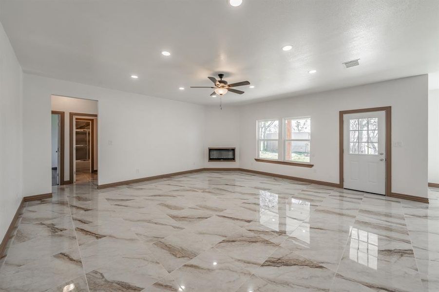 Unfurnished living room with recessed lighting, visible vents, baseboards, marble finish floor, and a glass covered fireplace