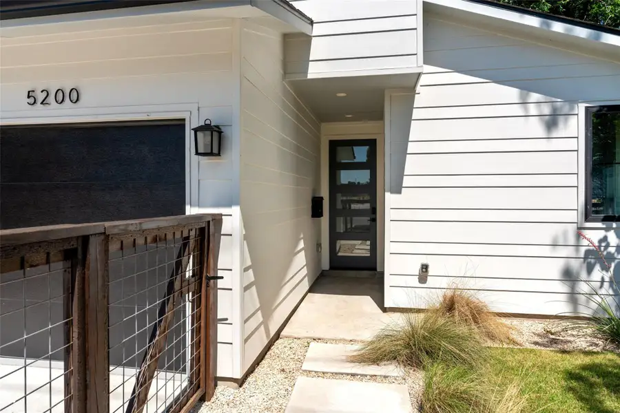 Contemporary white siding exterior featuring a dark paneled front door, an integrated garage, a concrete walkway, and a decorative wire-mesh gate. Contemporary white siding exterior featuring a dark paneled front door, an integrated garage, a concrete walkway, and a decorative wire-mesh gate.