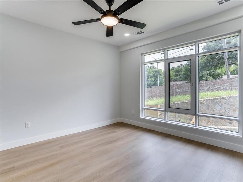 Expansive window in upstairs guest bedroom with wood-finish flooring, white baseboards, and a contemporary ceiling fan with integrated lighting Expansive window in upstairs guest bedroom with wood-finish flooring, white baseboards, and a contemporary ceiling fan with integrated lighting