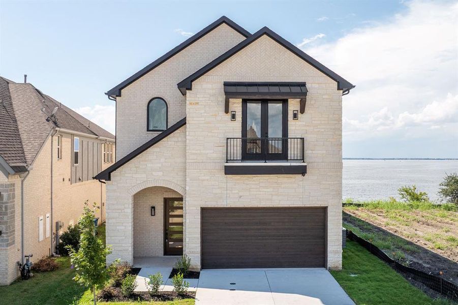 View of front of home with a balcony, stone siding, an attached garage, and driveway
