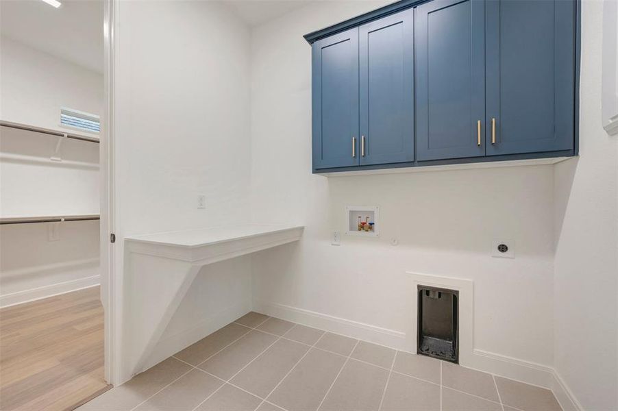 Practical utility room featuring blue wall-mounted cabinetry, a built-in countertop, and tiled flooring