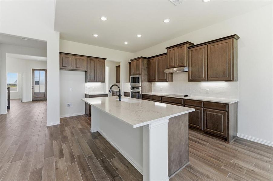 Kitchen featuring wood tiled floors, an island with sink, light stone counters, stainless steel appliances, and recessed lighting Kitchen featuring wood tiled floors, an island with sink, light stone counters, stainless steel appliances, and recessed lighting