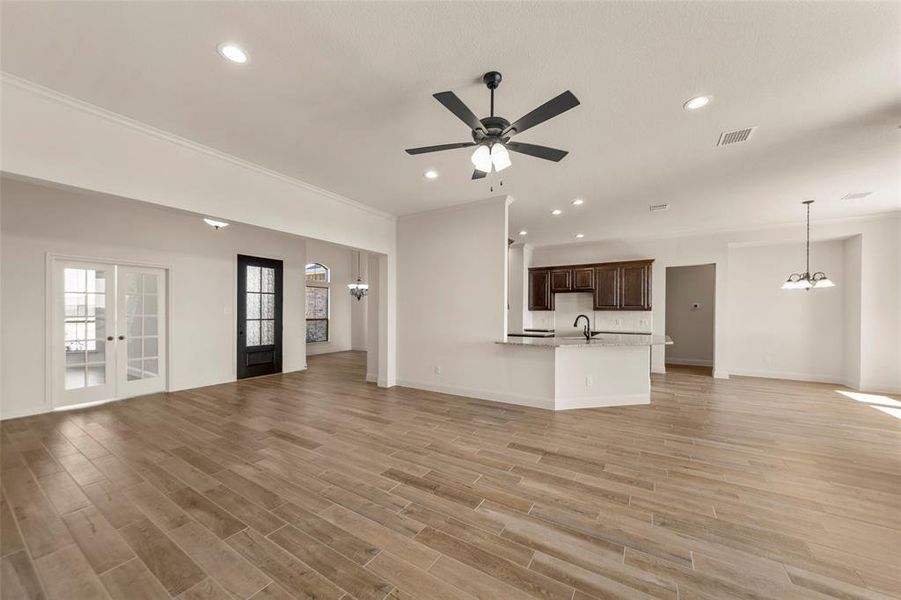 Unfurnished living room with a ceiling fan, wood finish floors, suspended lighting, french doors, and ornamental molding Unfurnished living room with a ceiling fan, wood finish floors, suspended lighting, french doors, and ornamental molding