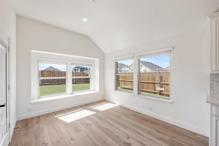Empty room with vaulted ceiling, hardwood floors, and large windows overlooking fenced backyard Empty room with vaulted ceiling, hardwood floors, and large windows overlooking fenced backyard