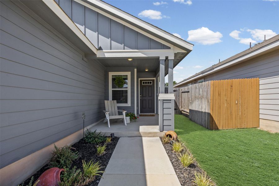 Concrete walkway leads to a covered front entryway flanked by siding and tidy landscaping.