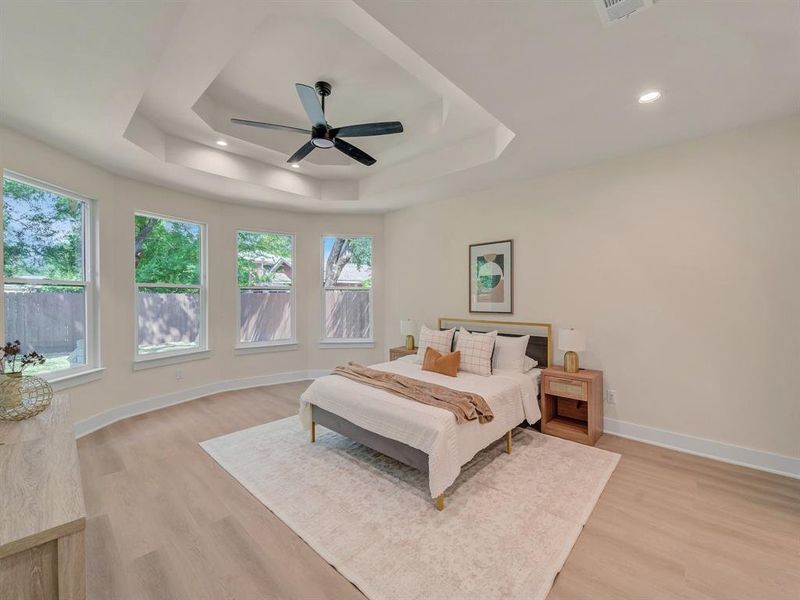 Bedroom featuring a raised ceiling, light hardwood / wood-style floors, and ceiling fan