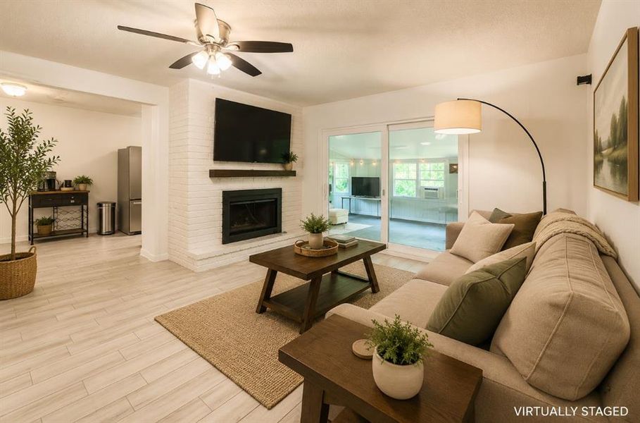 Living area featuring wood-finish flooring, a white brick fireplace with a dark wood mantel, and an overhead ceiling fan