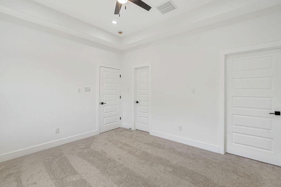 Alternate view of the primary suite highlighting the spacious layout and access points to the ensuite bathroom and dual closets.