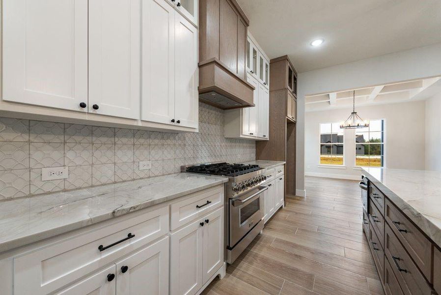 Kitchen featuring white cabinetry, light stone counters, backsplash, light hardwood / wood-style flooring, and high end stainless steel range