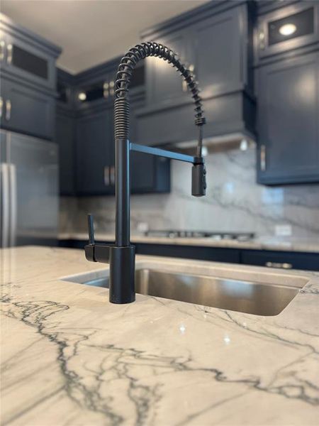 Room details featuring light stone counters, stainless steel refrigerator, glass insert cabinets, and a sink