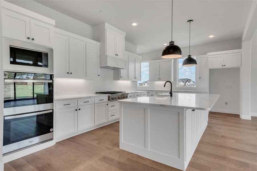 Kitchen with an island with sink, light hardwood / wood-style flooring, decorative light fixtures, white cabinetry, and stainless steel appliances