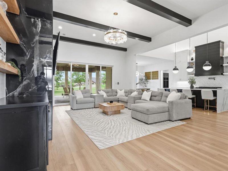 Spacious interior featuring high ceilings with dark exposed beams, light wood-finish flooring, and a contemporary chandelier