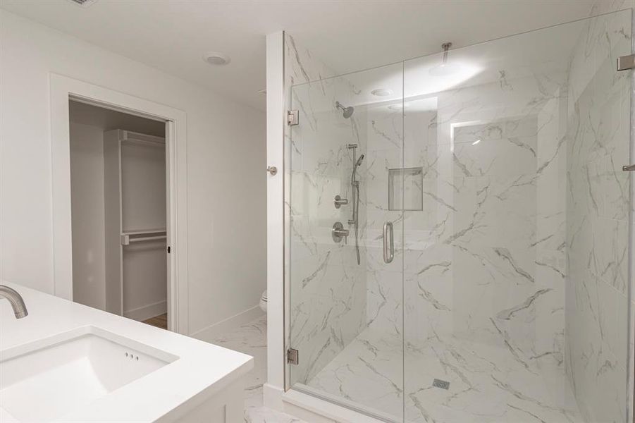 Bathroom featuring toilet, vanity, baseboards, marble finish floor, and a marble finish shower