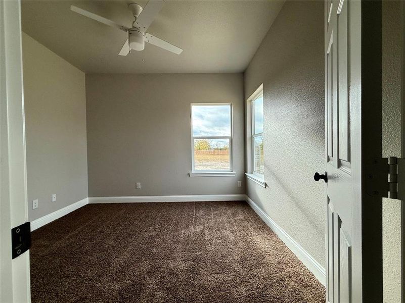 Unfurnished room featuring dark carpet, a ceiling fan, and a textured wall