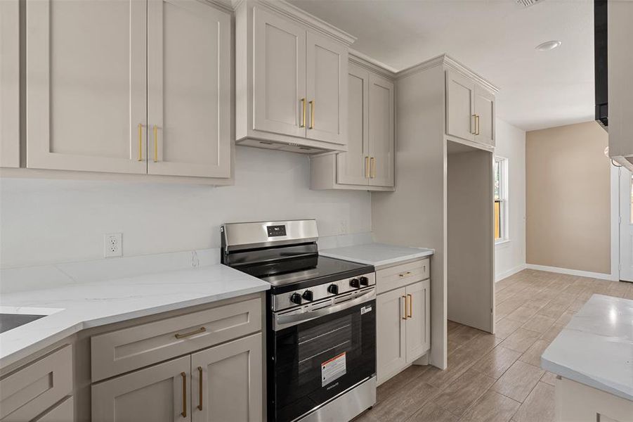 Kitchen featuring light-toned cabinetry with gold-toned hardware, white solid surface countertops, and a stainless steel electric range