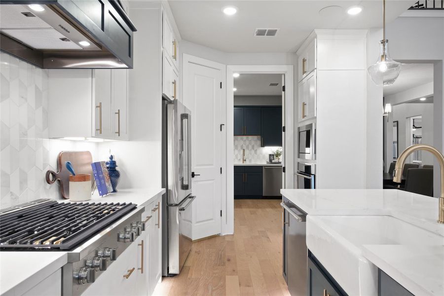 Kitchen with extractor fan, stainless steel appliances, decorative light fixtures, light wood-style flooring, and light stone counters