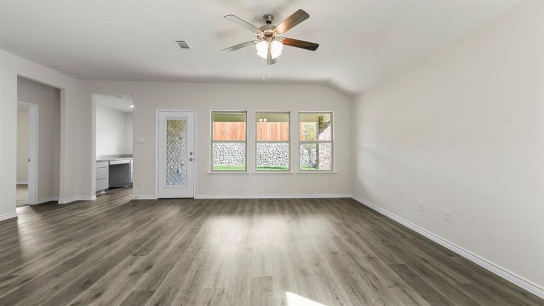 Expansive living area with wood-finish flooring, vaulted ceiling, and a ceiling fan