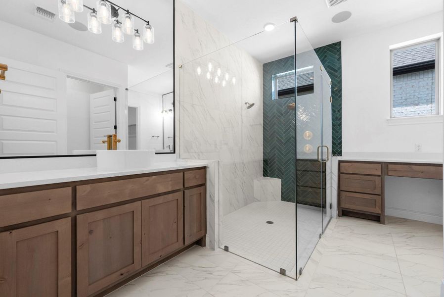Luxurious primary bathroom with dual vanities, beautiful countertops, and a spacious glass-enclosed shower.