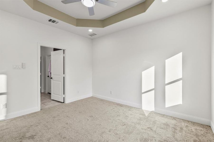 Carpeted empty room with a tray ceiling and ceiling fan