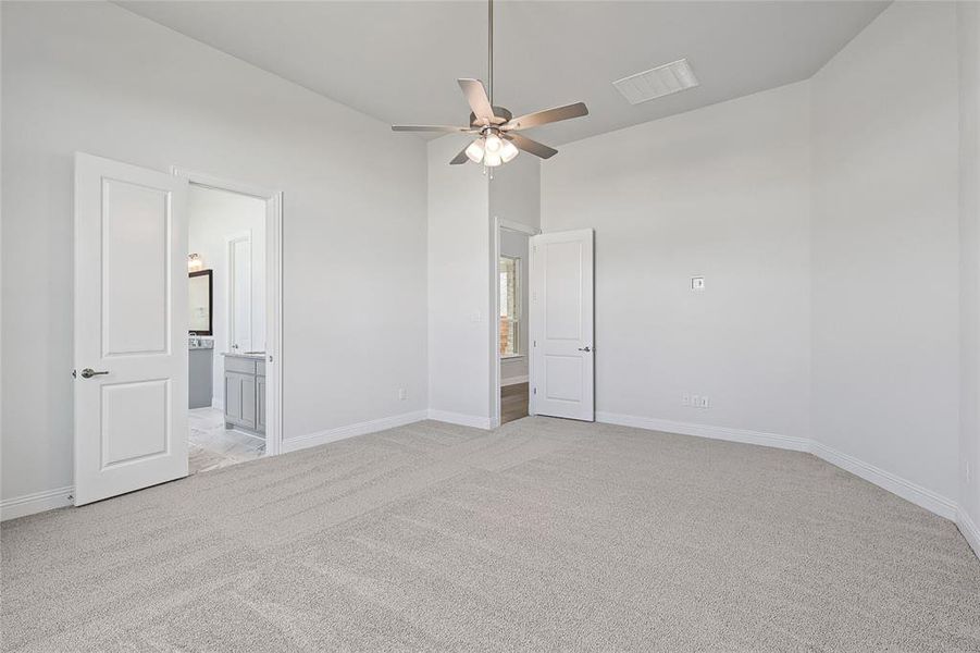 Unfurnished bedroom featuring light carpet, a ceiling fan, ensuite bathroom, and a high ceiling Unfurnished bedroom featuring light carpet, a ceiling fan, ensuite bathroom, and a high ceiling