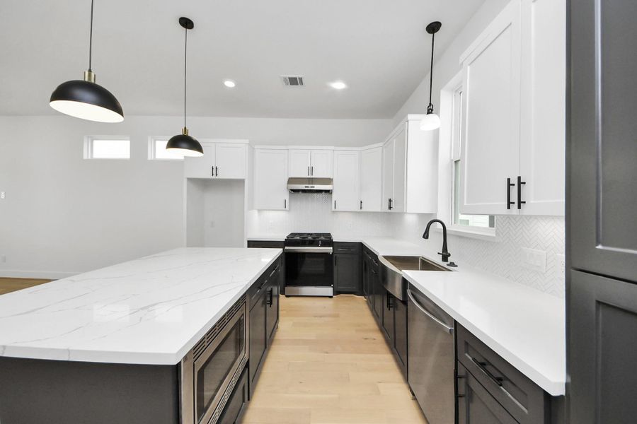 This modern kitchen features sleek white cabinetry with black accents, a spacious central island with a marble-like countertop, and stainless steel appliances. The room is well-lit with pendant lights and natural light from small windows, creating a bright and inviting space. This modern kitchen features sleek white cabinetry with black accents, a spacious central island with a marble-like countertop, and stainless steel appliances. The room is well-lit with pendant lights and natural light from small windows, creating a bright and inviting space.