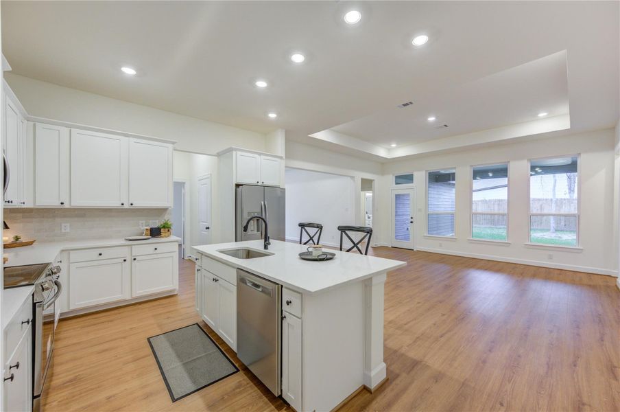 This spacious kitchen has sleek white cabinetry, a central island with modern fixtures, and seamlessly flows into a bright, open living area with expansive windows and warm wood flooring—perfect for entertaining and family gatherings. This spacious kitchen has sleek white cabinetry, a central island with modern fixtures, and seamlessly flows into a bright, open living area with expansive windows and warm wood flooring—perfect for entertaining and family gatherings.