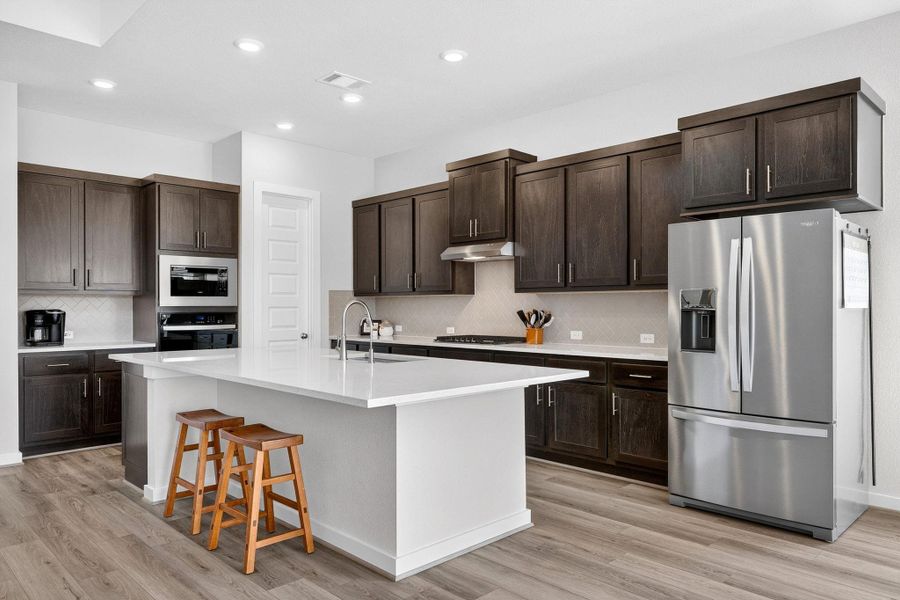Kitchen with stainless steel appliances, dark wood finish cabinets, quartz countertops and wrap-around breakfast bar area for plenty of seating.