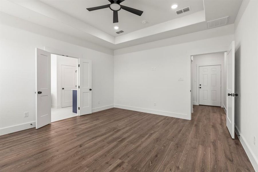 Unfurnished bedroom featuring dark wood finished floors, a tray ceiling, recessed lighting, and ceiling fan