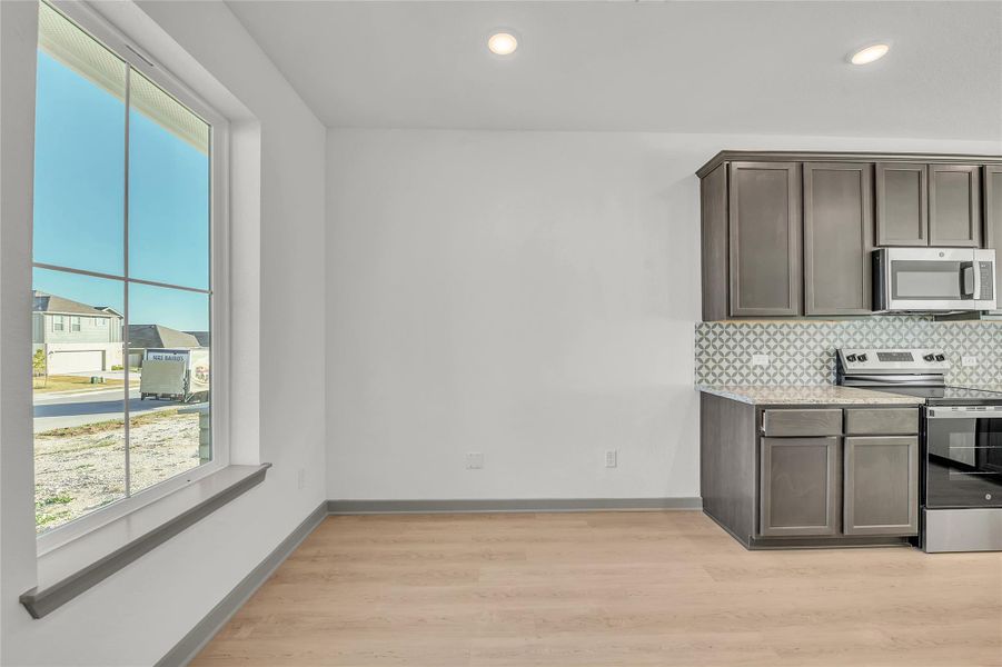 Kitchen featuring stainless steel appliances, light wood-style flooring, light stone countertops, dark wood finish cabinetry, and decorative backsplash