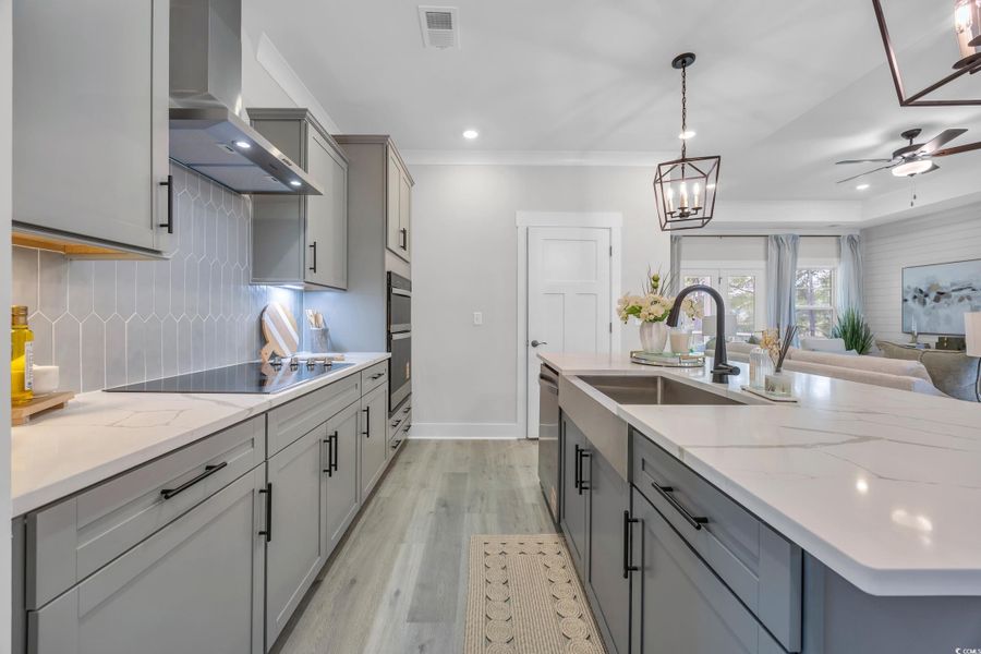 Kitchen featuring gray cabinetry, light wood finished floors, light stone counters, decorative light fixtures, and wall chimney range hood