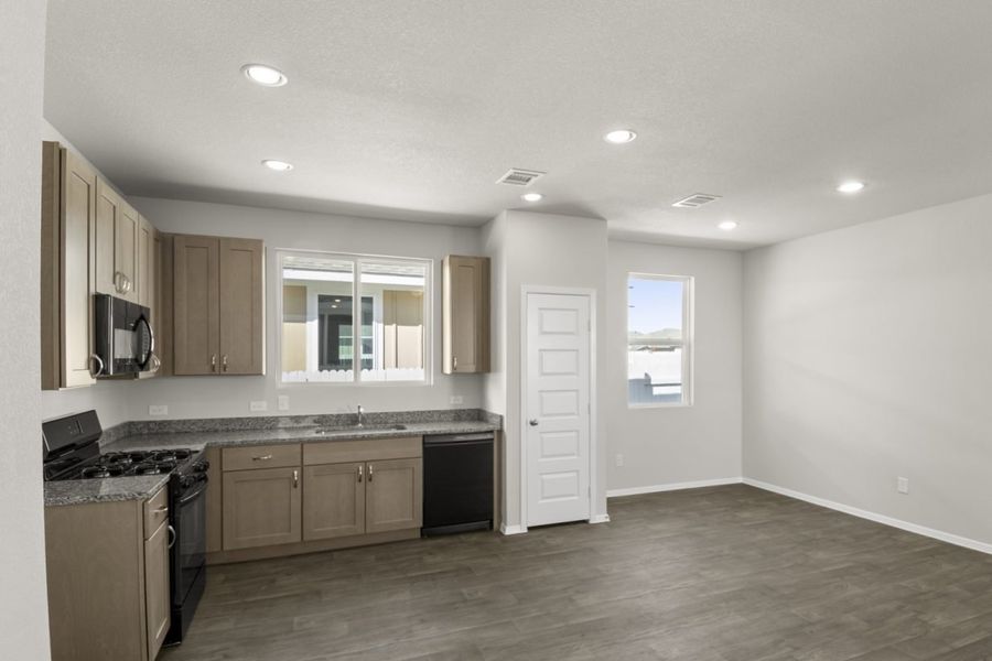 Image of a kitchen and dining room area with an L-shaped kitchen, dark. brown vinyl flooring, light grey walls and a window