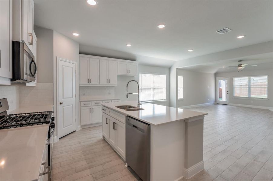 Open-concept kitchen and living area featuring a central island, white cabinetry, integrated stainless steel appliances, and wood-finish tile flooring