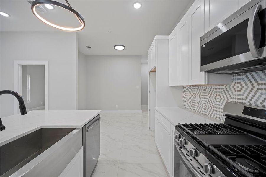 Kitchen with light stone counters, decorative backsplash, marble finish floor, stainless steel appliances, and a sink