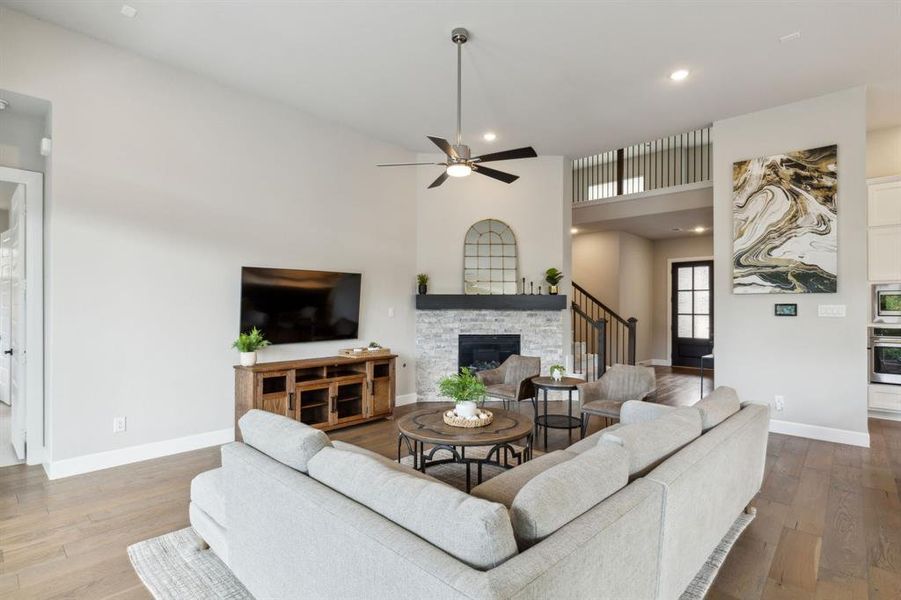 Living room with high vaulted ceiling, ceiling fan, hardwood / wood-style flooring, and a stone fireplace