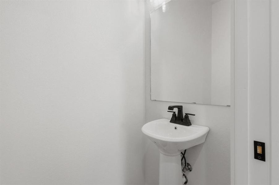 Bathroom featuring a white pedestal sink with a matte black faucet, and a wall-mounted mirror