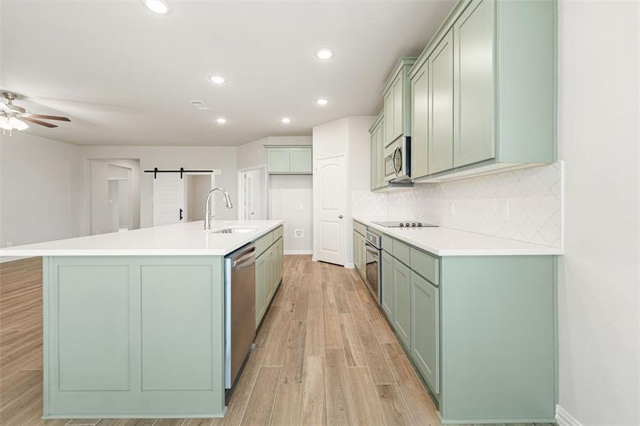 Kitchen with green cabinetry, a barn door, light wood finished floors, recessed lighting, and tasteful backsplash Kitchen with green cabinetry, a barn door, light wood finished floors, recessed lighting, and tasteful backsplash