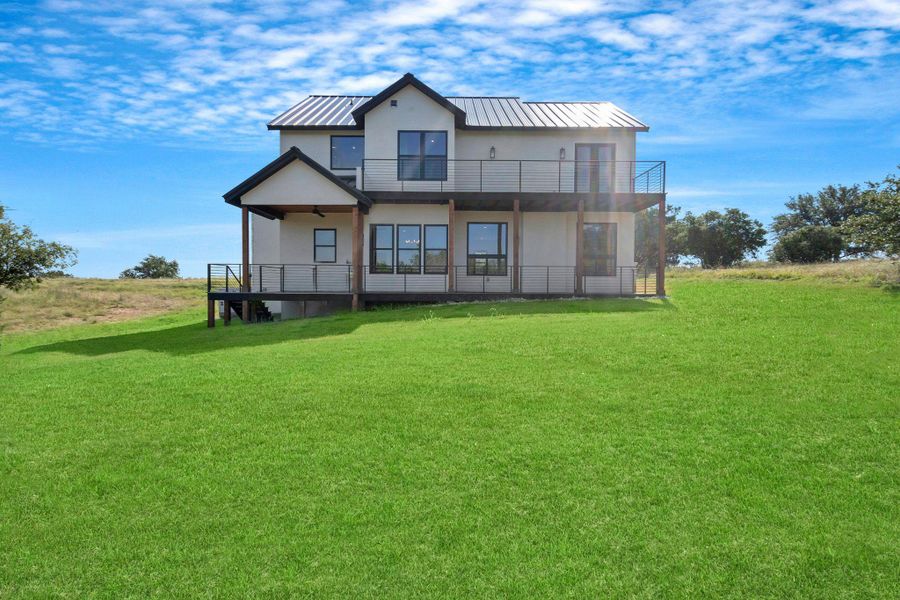 Back of property with a balcony, metal roof, a standing seam roof, a yard, and stucco siding Back of property with a balcony, metal roof, a standing seam roof, a yard, and stucco siding